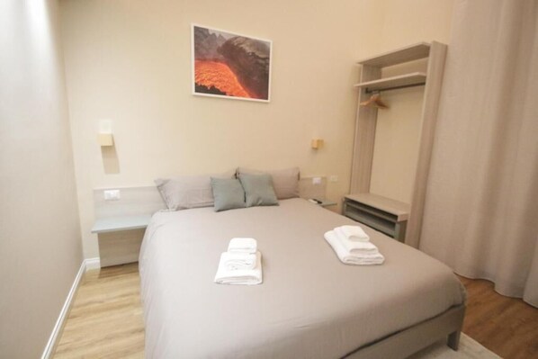 A hotel room with a bed, a bench, a coat rack, and a painting on the wall. - Etna Vibes Home (Catania)