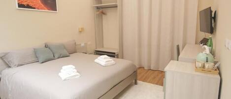 Quarto de hotel com cama, mesa de cabeceira, espelho, televisão e janela com cortinas.