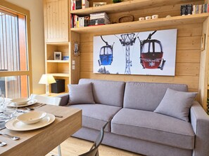 A cozy living room with a sofa, a dining table set with plates and cutlery, a lamp, and a bookshelf filled with books. - Renovated apartment, mountain view - 4 guests (Courchevel 1650)