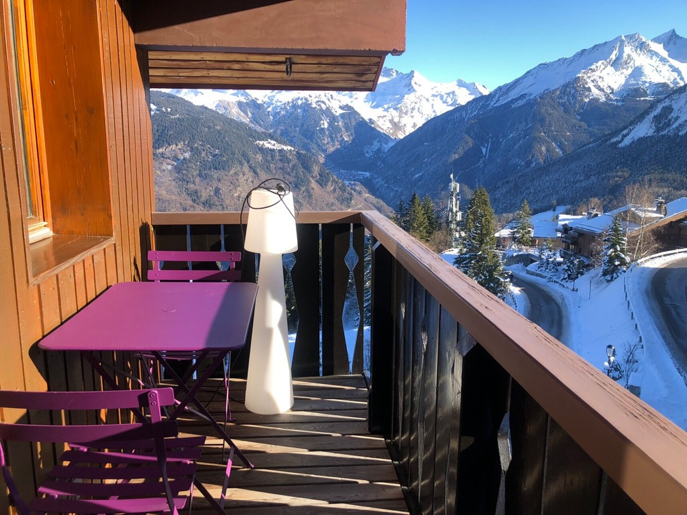 A wooden balcony with a purple table and chairs, overlooking a snowy mountain landscape.
