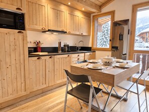 A wooden kitchen with a dining table set for four, a microwave, and a window with a snowy view. - Renovated apartment, mountain view - 4 guests (Courchevel 1650)