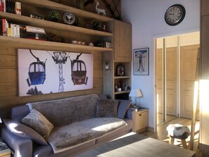 A cozy living room with a sofa, a coffee table, a bookshelf, and a wall clock.