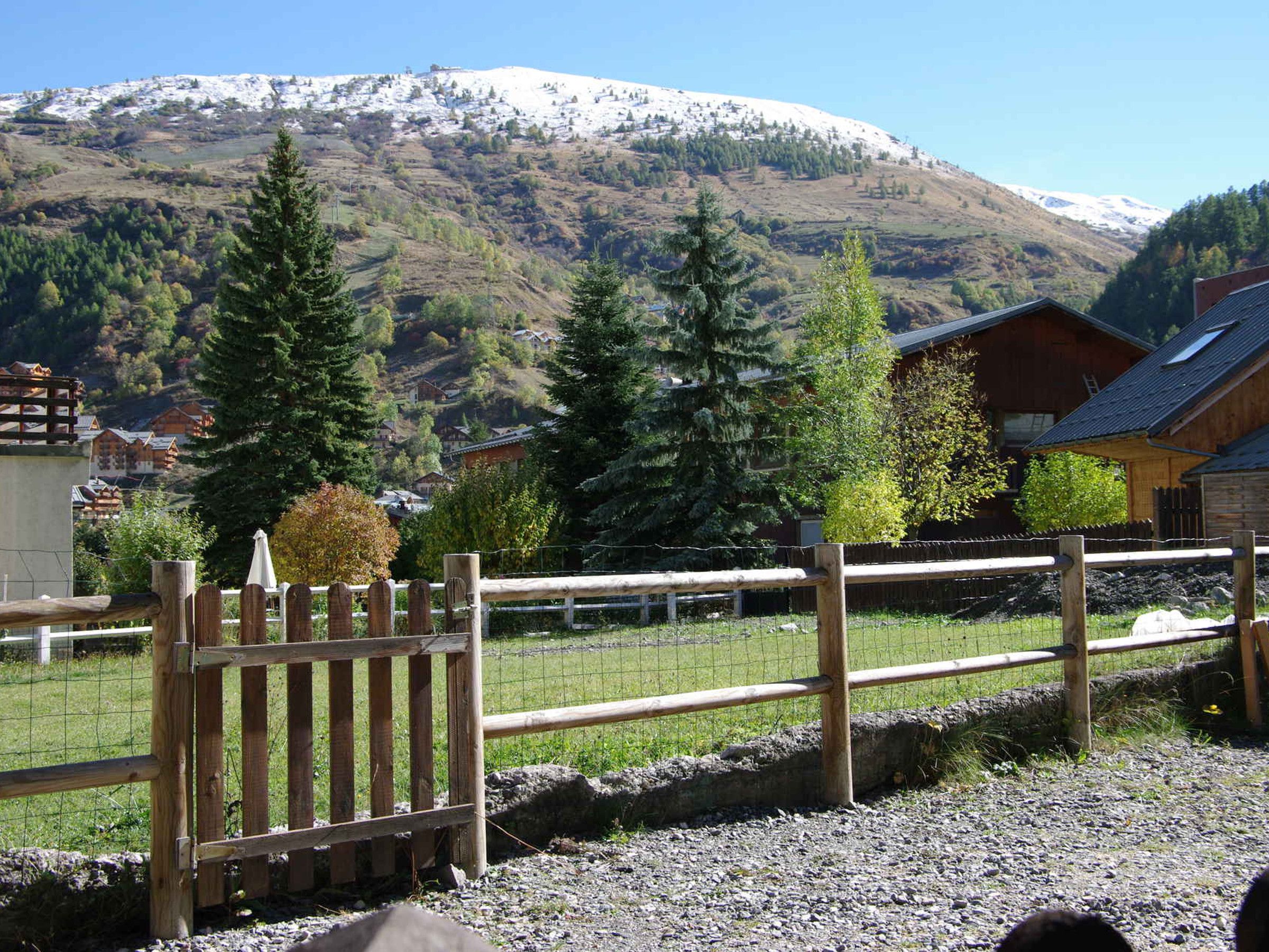 Une clôture en bois avec un portail, un paysage montagneux en arrière-plan et un bâtiment doté d’un toit en pente.