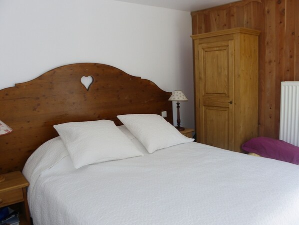 A bedroom with a wooden headboard, a bed with white bedding, a nightstand with a lamp, and a wooden wardrobe. - Practical apartment in Valloire - 5 guests (Valloire)