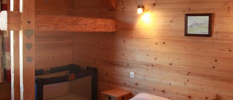 A wooden room with a bunk bed, a small bedside table, and a wall-mounted light fixture.