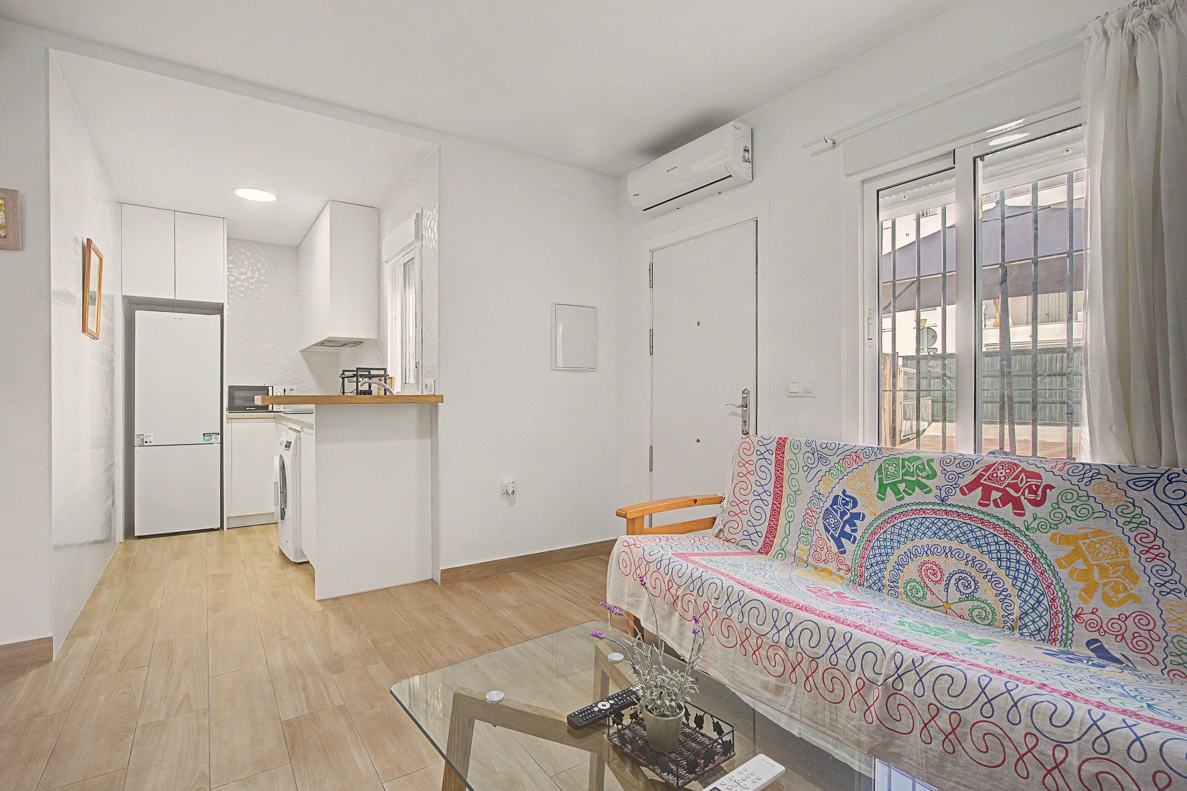 Uma sala de estar moderna com um sofá, uma mesa de centro de vidro e uma área de cozinha ao fundo.