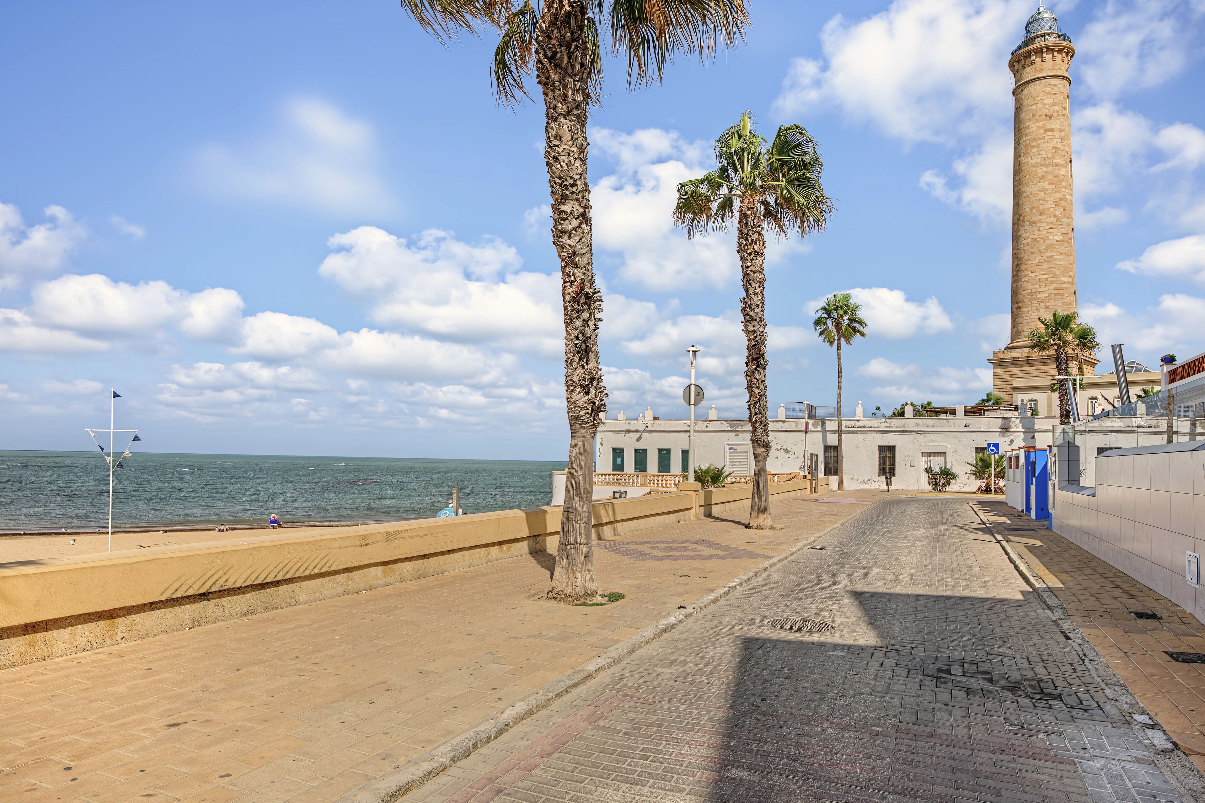 A coastal promenade with palm trees, a lighthouse, and a view of the sea.