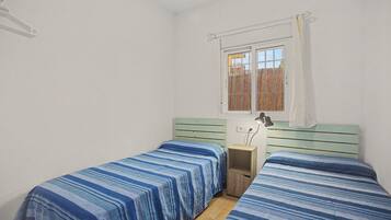 Ein Schlafzimmer mit zwei Einzelbetten, einem Fenster mit Blick auf einen Zaun und einem kleinen Nachttisch mit einer Lampe.