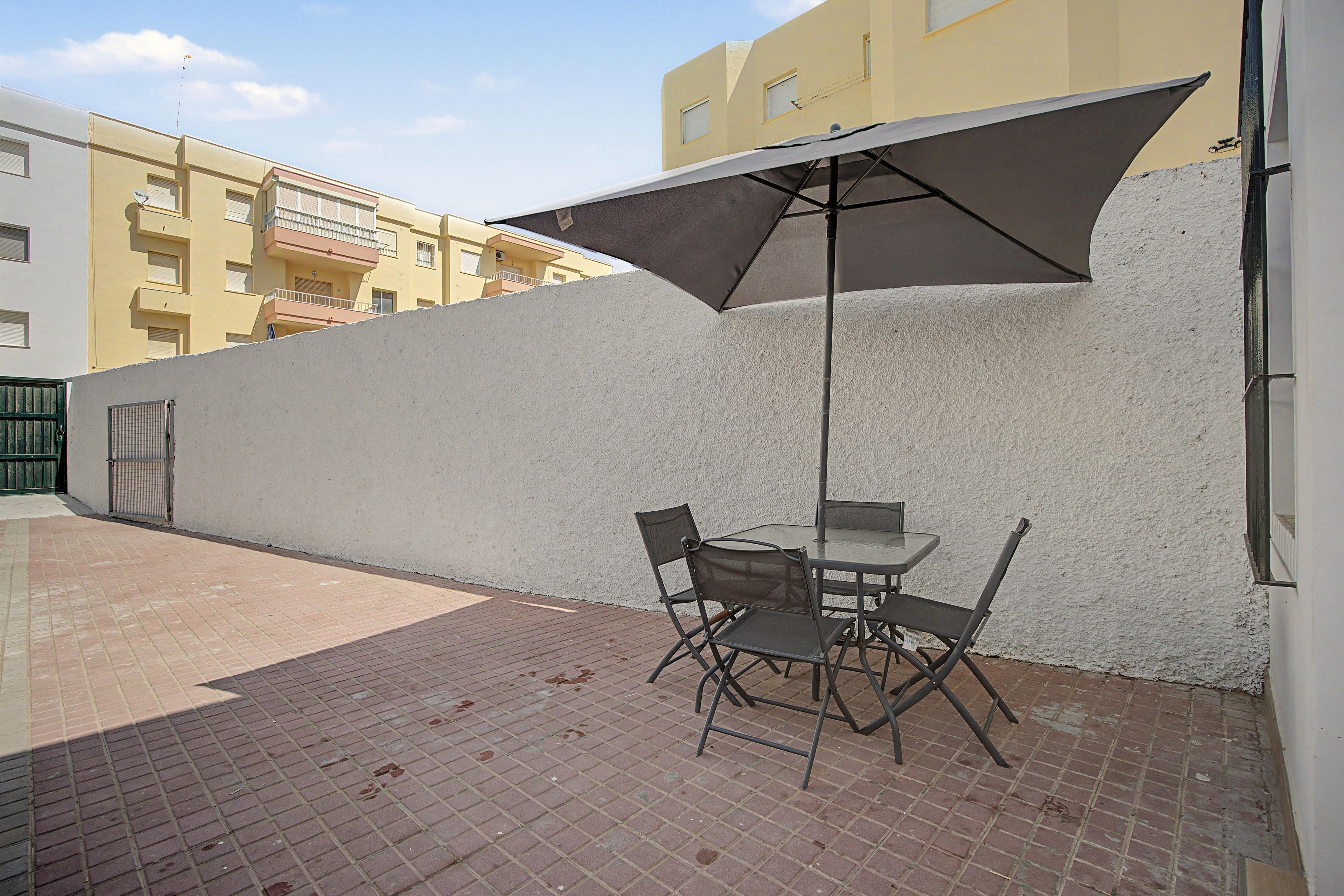 Un espace extérieur aménagé en terrasse, avec une table et des chaises, un grand parasol et un sol en briques.