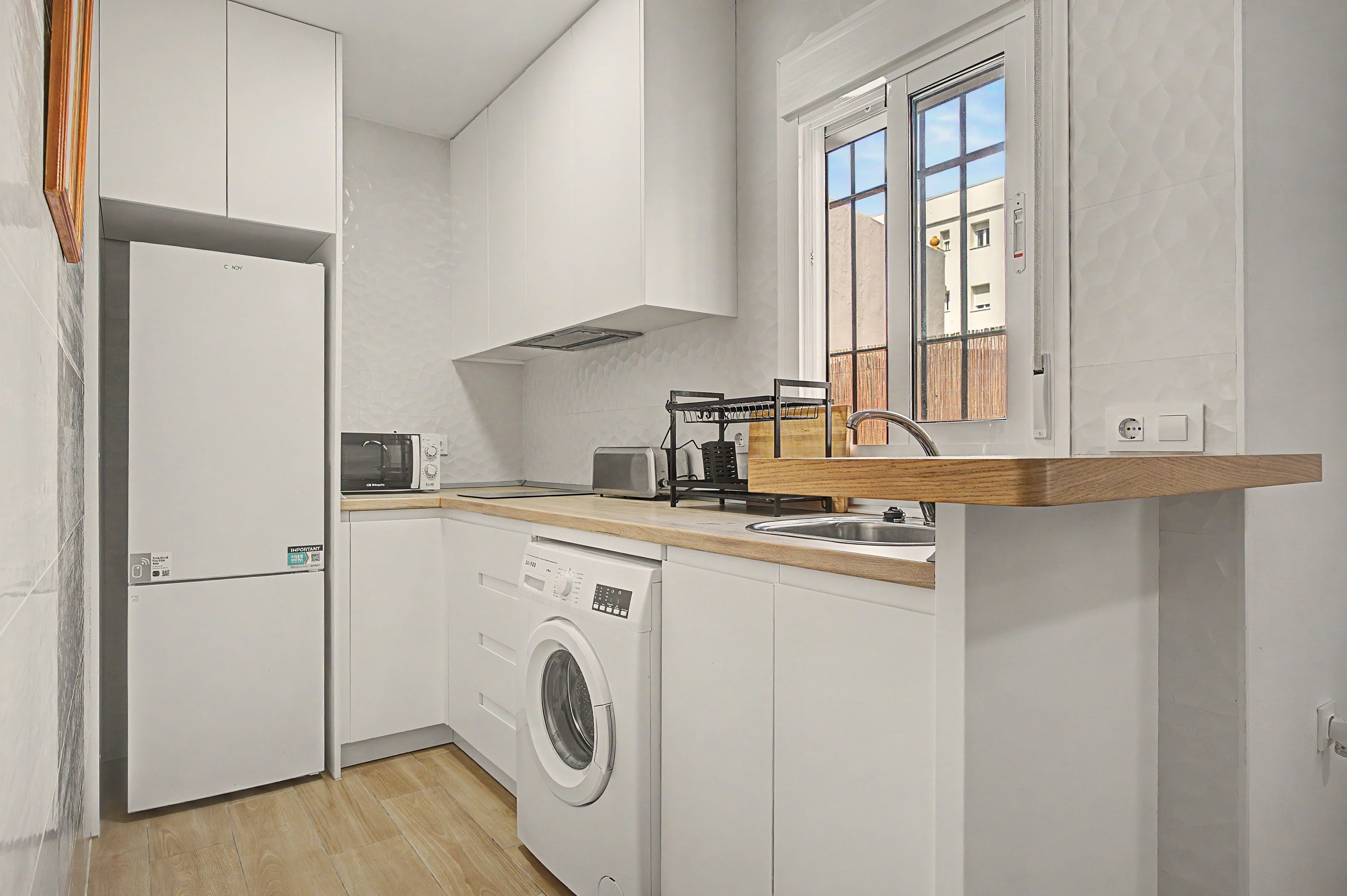 Une cuisine compacte équipée d’un lave-linge intégré, d’un four à micro-ondes et d’un plan de travail en bois.