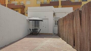 A narrow courtyard with a table and chairs, a door, and a small covered area with an umbrella.