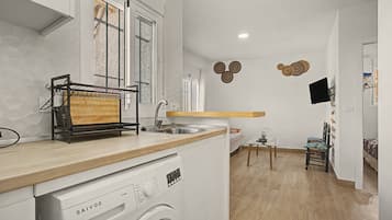 A compact kitchen with a built-in washer, a window with blinds, and a small dining area.