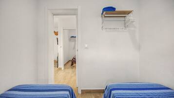 A room with two beds, a wooden floor, a white door, and a small shelf with a towel.