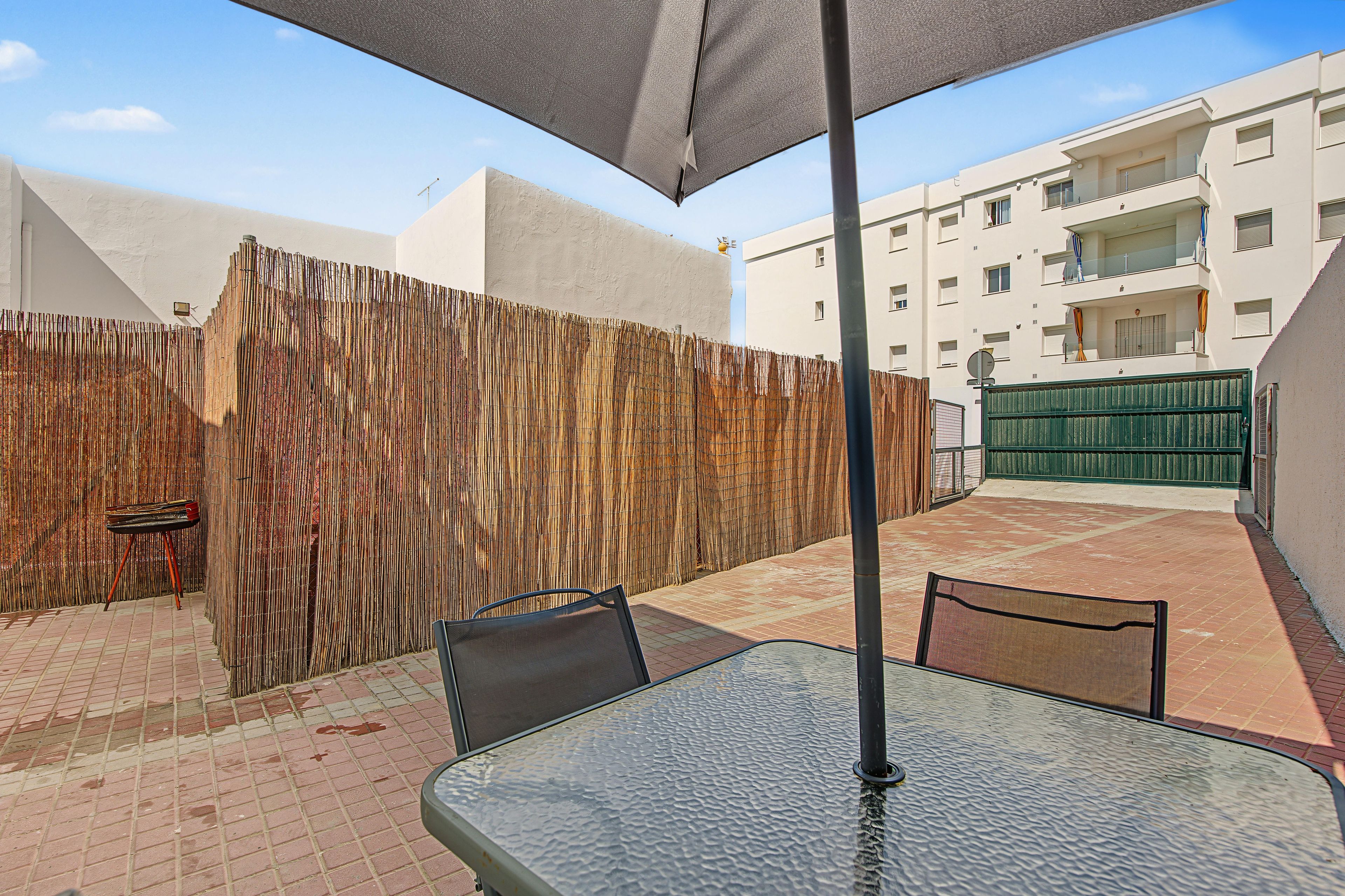 Un patio al aire libre con una mesa y sillas, una cerca de bambú y un edificio al fondo.