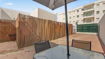 Un patio al aire libre con una mesa y sillas, una cerca de bambú y un edificio al fondo.