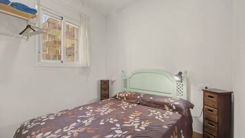 Ein Schlafzimmer mit einem Bett, einem Fenster, einem Kleiderschrank und einem an der Wand befestigten Regal mit Handtüchern.