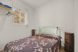 Ein Schlafzimmer mit einem Bett, einem Fenster, einem Kleiderschrank und einem an der Wand befestigten Regal mit Handtüchern.
