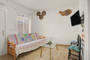 Un saló amb un sofà, una taula de café de vidre, un televisor fixat a la paret i una taula petita amb objectes decoratius.