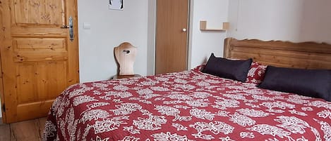 A bedroom with a wooden door, a bed with a patterned bedspread, a bedside lamp, and a wall-mounted picture.