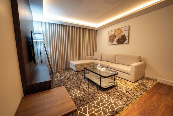 A modern living room with a sectional sofa, a glass coffee table, a wooden side table, and a patterned floor.