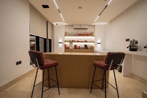 A modern kitchen with a bar area, two bar stools, and a coffee station.