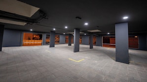A spacious indoor parking area with multiple columns, marked parking spaces, and a visible entrance to a building with barred windows.