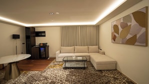 A modern living room with a sectional sofa, a glass coffee table, a dining table, and a patterned rug.