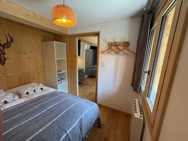 A bedroom with a bed, a hanging light fixture, a wardrobe, a mirror, and a window. - 3* Apartment, south, parking - 5 guests (Valloire)