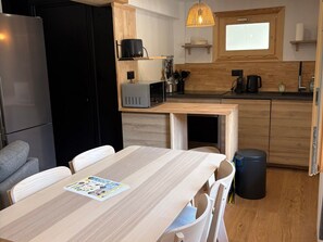 A compact kitchen with a microwave, stove, and sink. There is a dining table with chairs and a magazine on it. - 3* Apartment, south, parking - 5 guests (Valloire)