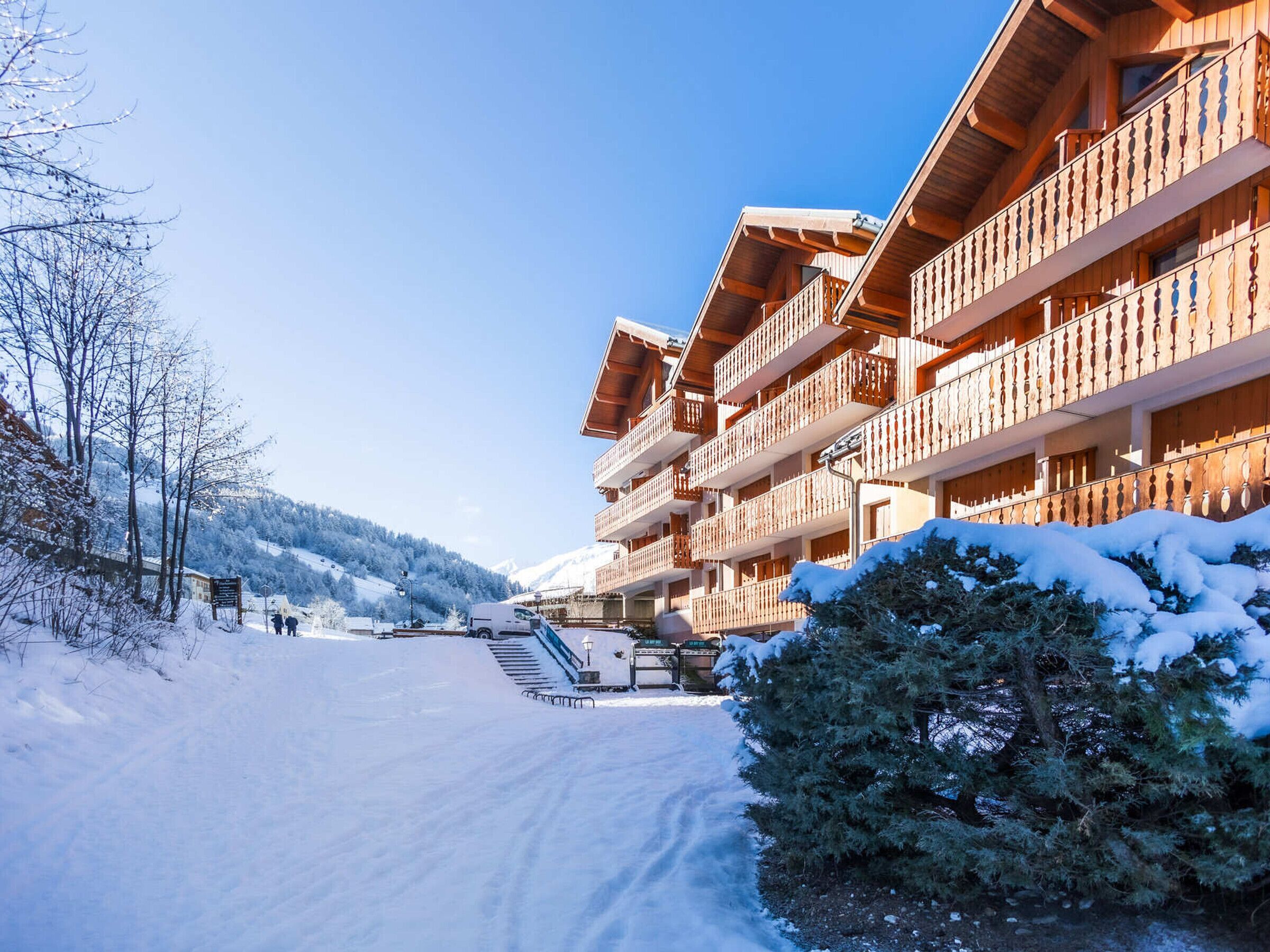 A wooden building with balconies, a snow-covered path, and a mountain in the background.