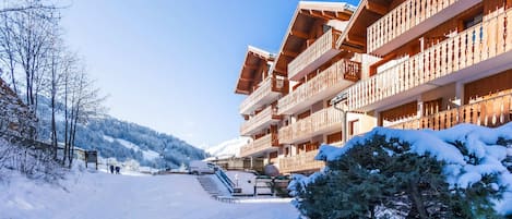 A wooden building with balconies, a snow-covered path, and a mountain in the background.