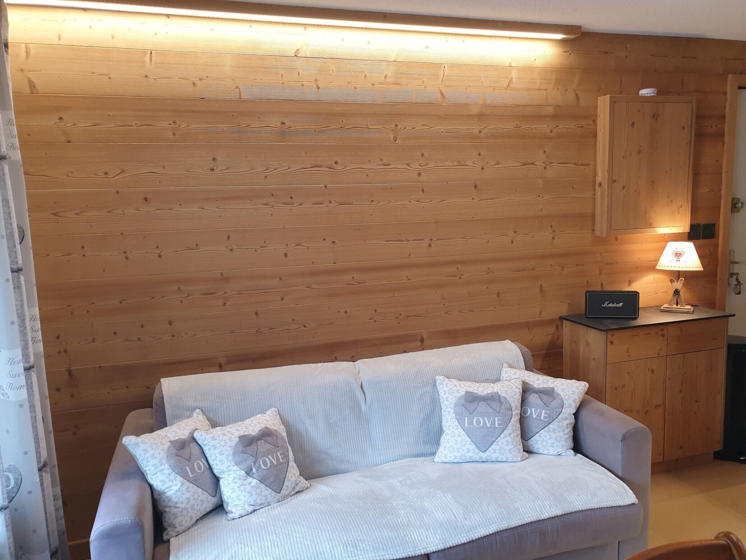 Une pièce avec un mur en bois, un canapé agrémenté de coussins à motifs, une petite table avec une lampe et un meuble.