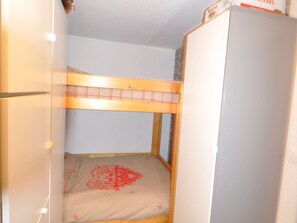 Ein Stockbett mit Holzrahmen und einer Matratze mit rotem Muster.
