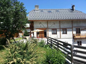 En traditionell chalet med ett sluttande tak, en träbalkong och en skorsten av sten.