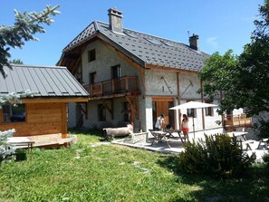 A two-story wooden house with a balcony, a patio area, and a small wooden structure. - Spacious triplex - 12 guests southwest view (Valloire)