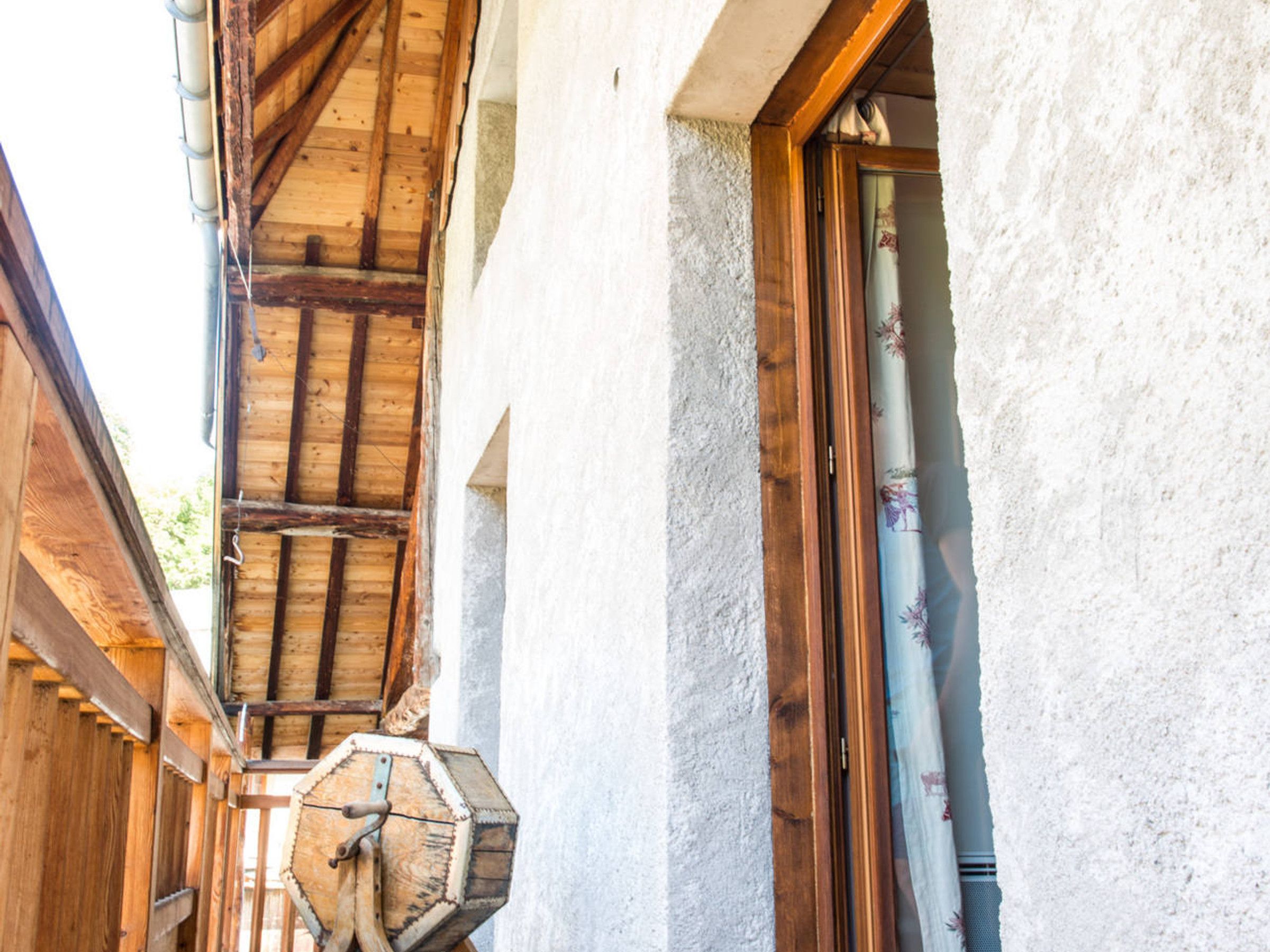 Eine Holztreppe führt zu einem Balkon, einer sechseckigen Holzkonstruktion und einem Fenster mit Vorhang.