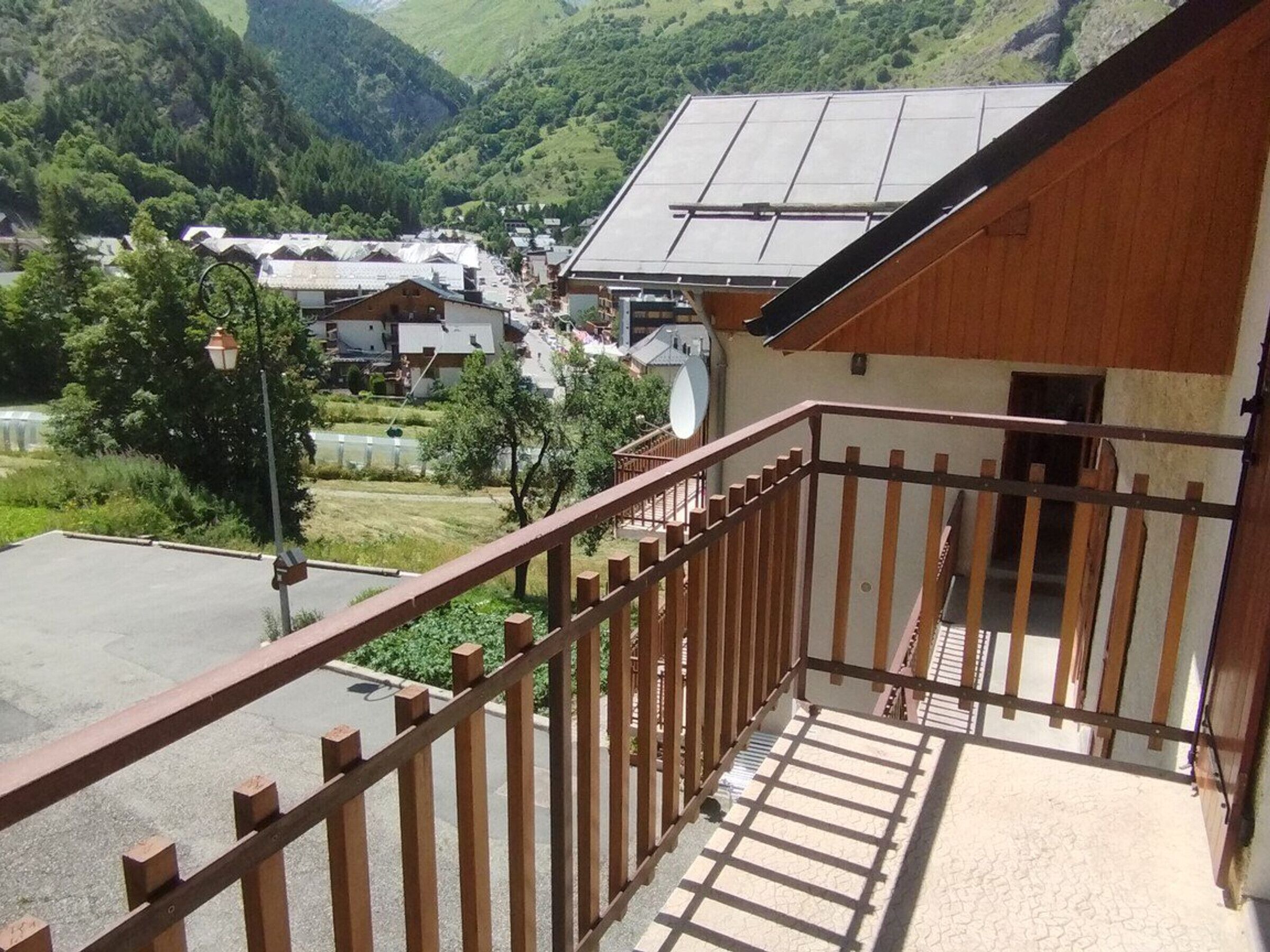 Een balkon met houten spijlen met uitzicht op een vallei met huizen en groen.