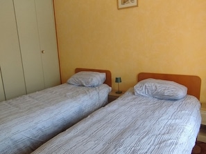 Ein Zimmer mit zwei Einzelbetten, jeweils mit Kissen und einem kleinen Nachttisch mit Lampe.