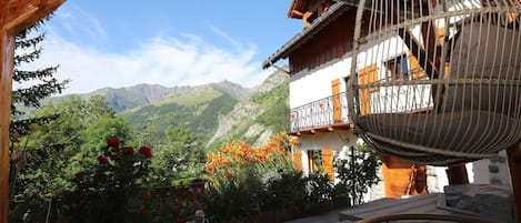 A wooden balcony with a hanging chair, overlooking a mountainous landscape.