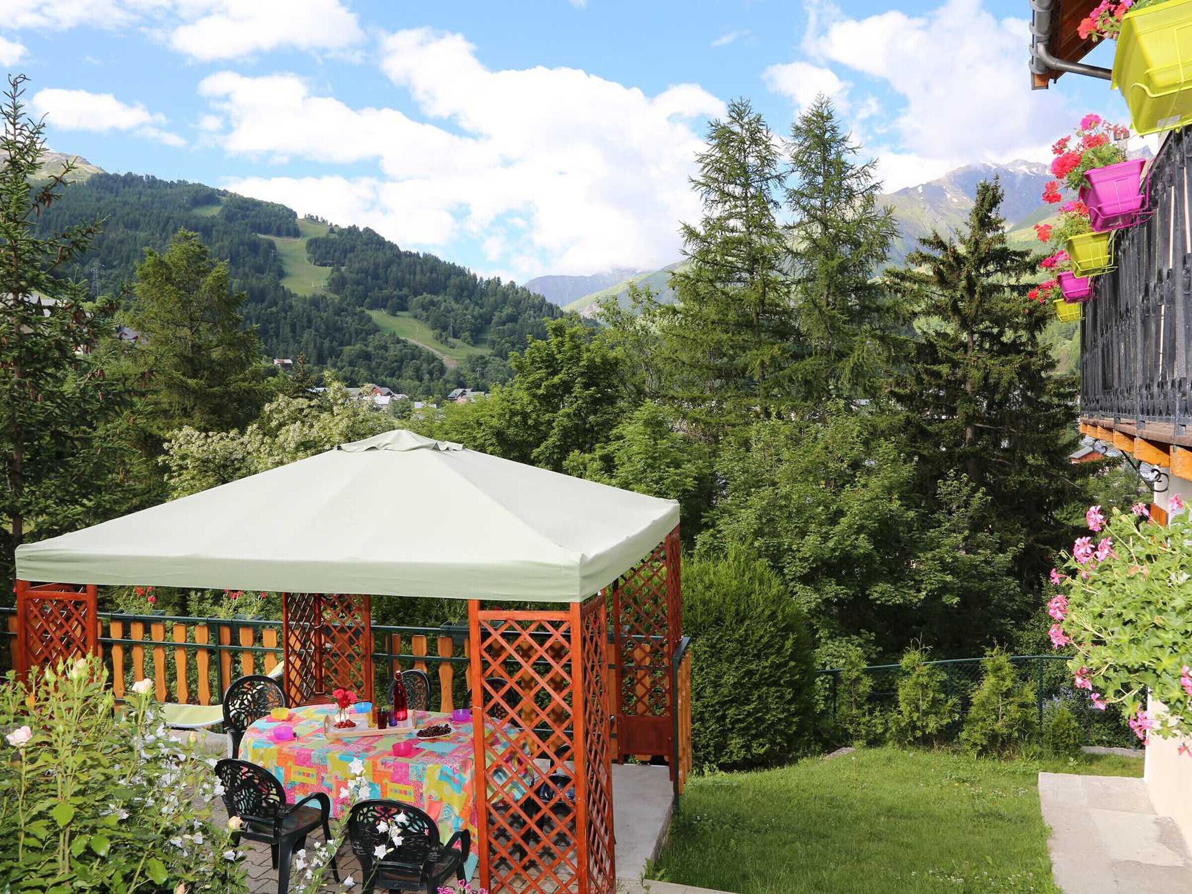 Un belvédère abritant une table et des chaises, entouré de verdure et avec une chaîne de montagnes en arrière-plan.