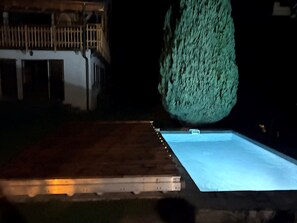 Ein Schwimmbecken mit einer Holzterrasse und einem hohen Baum im Hintergrund.
