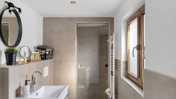 Ein modernes Badezimmer mit Waschbecken, Spiegel, Handtuchhalter und Duschbereich.