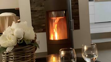A modern interior with a wood-burning stove, a wicker basket with flowers, and two wine glasses on a tray.