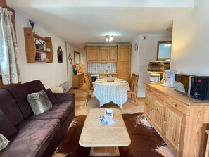 En hyggelig stue med en sofa, et sofabord og et spiseområde med et bord dækket til to personer.