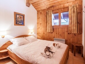 Ein Zimmer mit Holzwand, ausgestattet mit einem Bett, einem Nachttisch, einer Lampe, einem Fenster mit Vorhängen und einem Bild an der Wand.