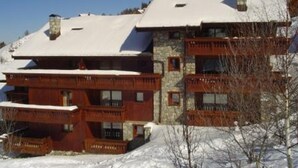 Un edifici d'alguns pisos amb balcons, envoltat de terra i arbres coberts de neu.