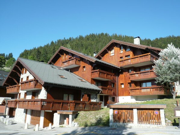 A wooden chalet-style building with multiple balconies and a sloped roof, surrounded by a forested area. - Cozy apartment, parking - 4 guests (Méribel)