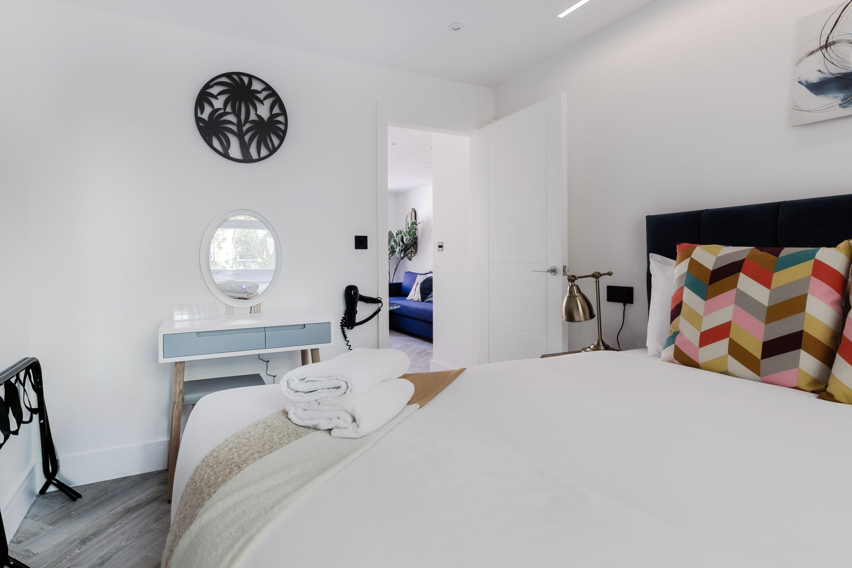 A modern hotel room with a bed, a vanity with a mirror, a hairdryer, and a view of the hallway.