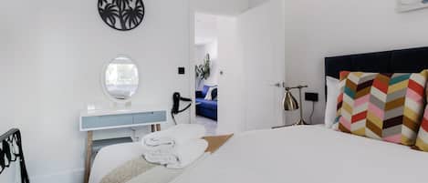 A modern hotel room with a bed, a vanity with a mirror, a hairdryer, and a view of the hallway.