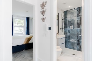 A modern bathroom with a glass shower enclosure, a white toilet, and a bed with a blue curtain. - Comfortable Apartments near Harrods (London)